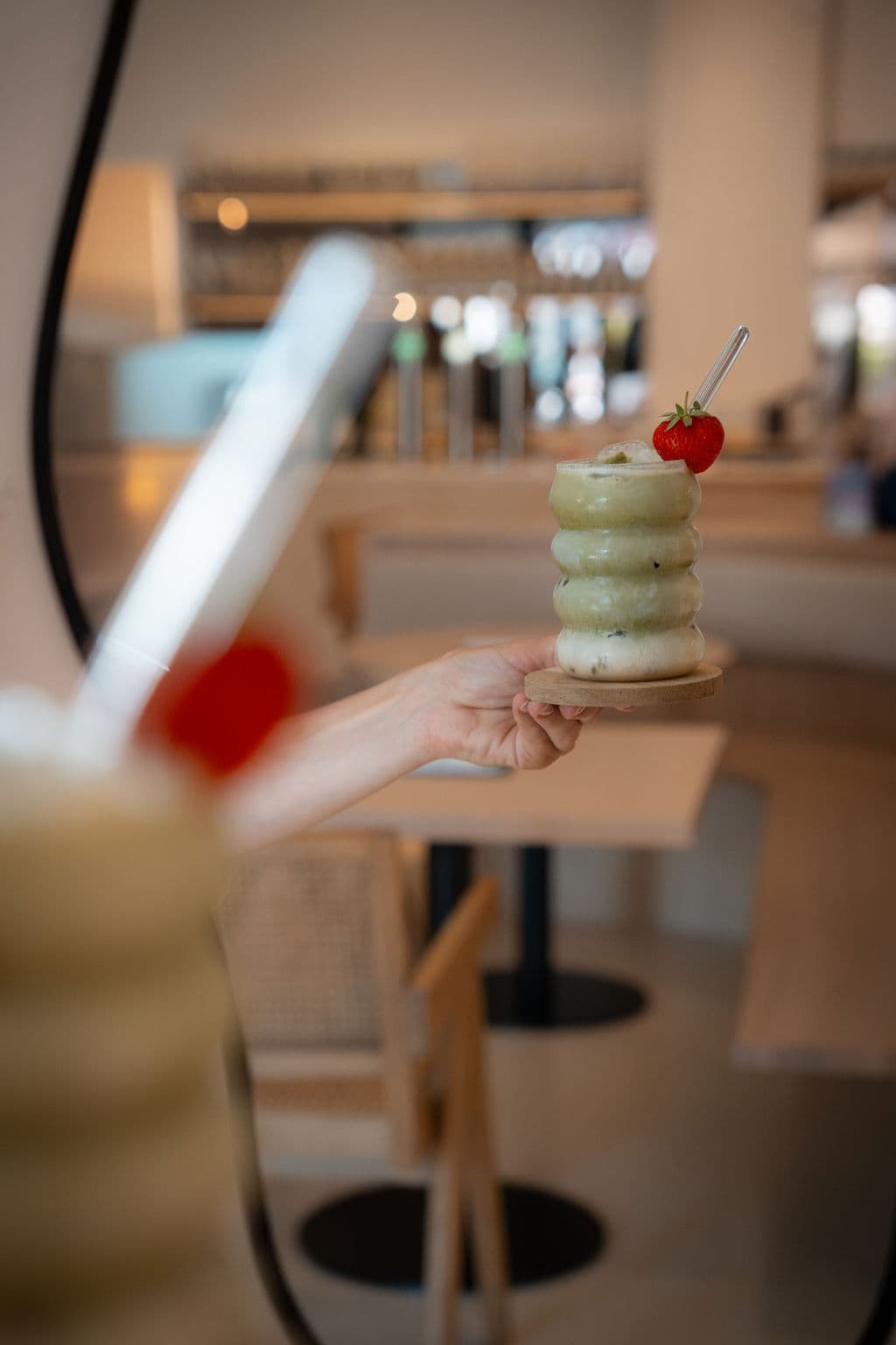 Frau im Café Hufschmiede hält eine Tasse mit kunstvoll zubereitetem Matcha Latte in der Hand, im Hintergrund ist die Bar zu sehen.